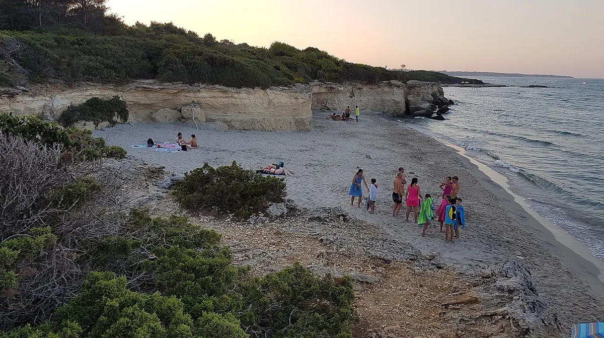 Tratto della spiaggia di Baia dei Turchi con sabbia, scogli e vegetazione costiera.