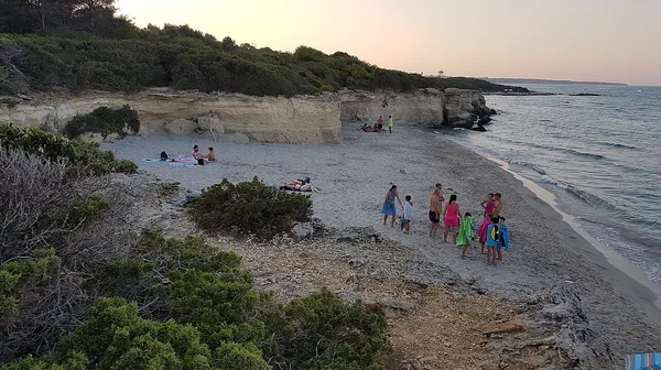 Tratto della spiaggia di Baia dei Turchi con sabbia, scogli e vegetazione costiera.
