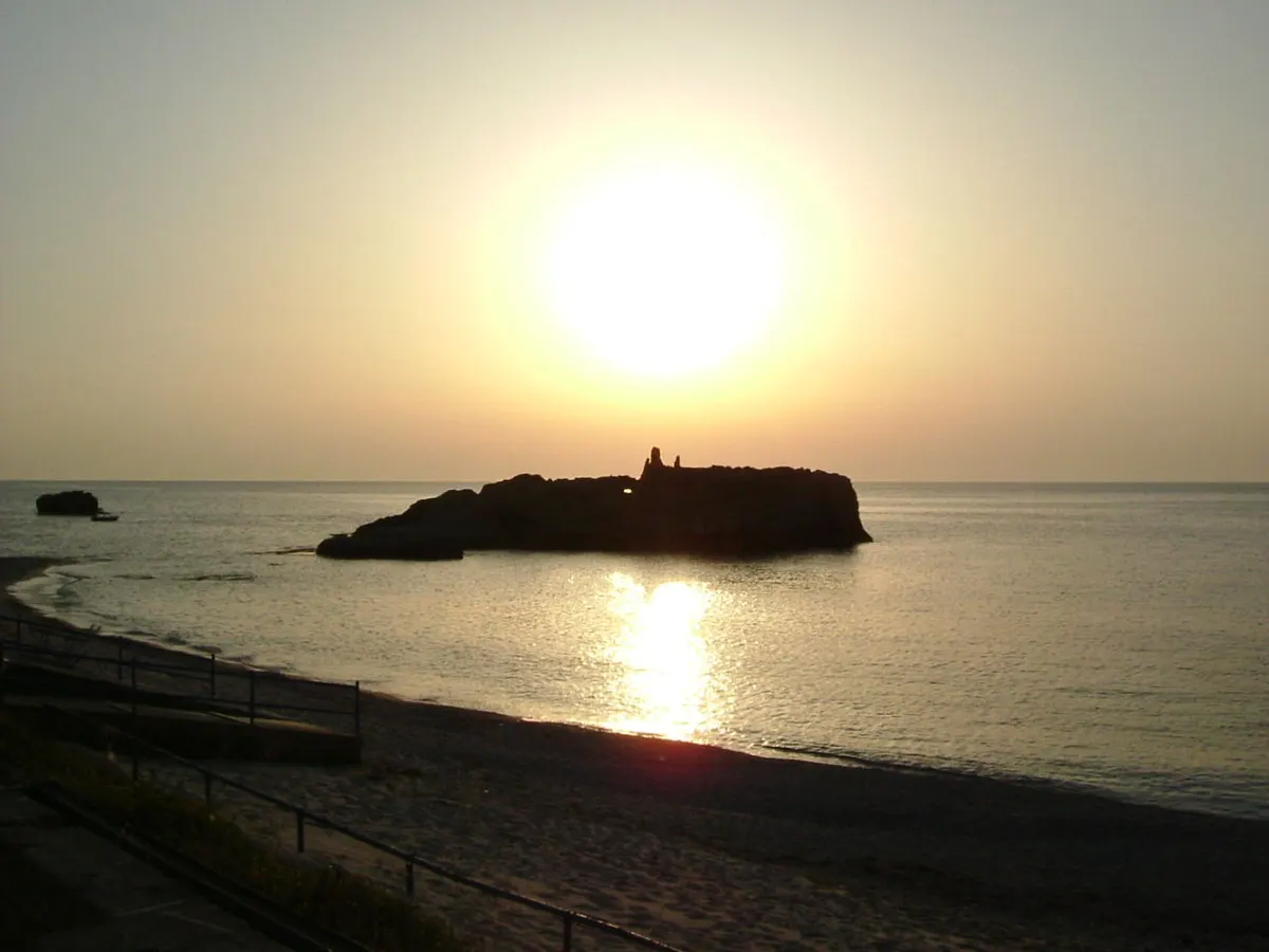 Lo scoglio della baia di Riaci al tramonto, con la riva in primo piano.